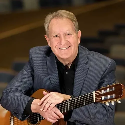 Professor Mike Christiansen holding a classical guitar for a testimonial on our effective eLearning development.